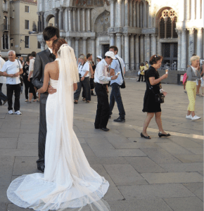 Couple in Wedding Attire in foreground as people pass by in background at St. Mark's Square in Venice