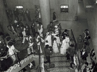 Black and white picture of wedding party on the stairs with bagpiper in background