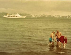 Three people in cold water with a cruise ship in the background experiencing a travel bucket list adventure in the antarctic.