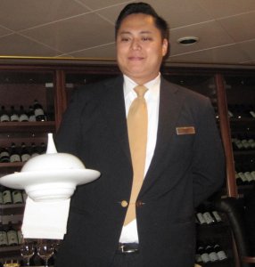 A server holding a white dish with a cover