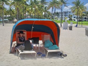 Woman laying on beach in Lago Mar under red tent with palm trees in background.