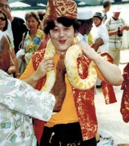 Man with large yellow snake around his neck wearing red and gold hat