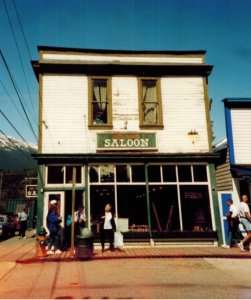 Image of saloon in Alaska, white two story building with green saloon sign outside