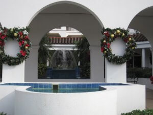 in ground pool in front of white archway with two Christmas wreaths on each side
