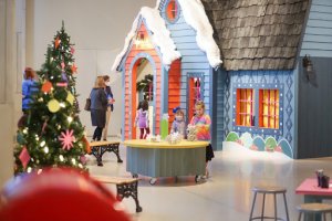 Blue house Inside museum with warm orange light coming through windows with Christmas tree outside and family entering